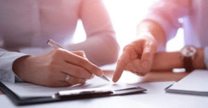 (Close-up of a person signing a legal document with guidance, representing professional help with debt settlement agreements.) 