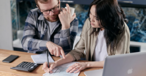(A couple sits at a table reviewing financial documents, calculator and laptop in front of them, highlighting a serious discussion about budgeting or managing debt.)
