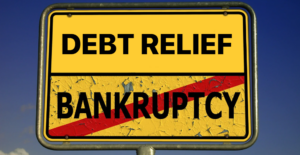A yellow road sign reads “Debt Relief” with “Bankruptcy” crossed out, symbolizing a shift from financial crisis to recovery. 