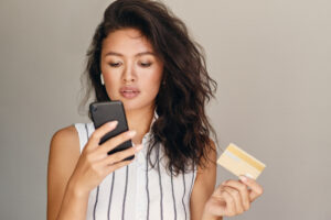 Woman reviewing her account balance on a smartphone with a credit card in hand.